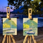 2 painting on the easels in the night. Each painting show the Lecco harbour during the sunset